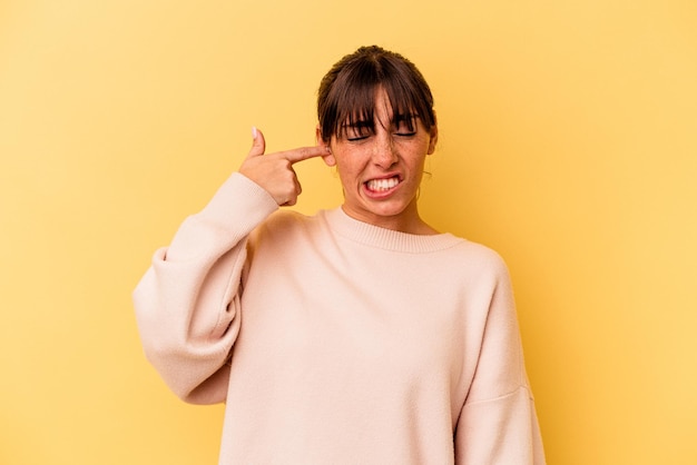 Jeune femme argentine isolée sur fond jaune couvrant les oreilles avec les mains.