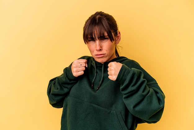 Jeune femme argentine isolée sur fond jaune montrant le poing à la caméra, expression faciale agressive.