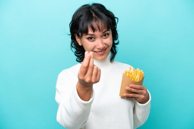 Jeune femme argentine tenant des frites frites isolées sur fond bleu faisant un geste d'argent