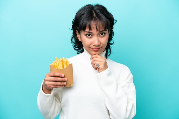 Jeune femme argentine tenant des frites frites isolées sur fond bleu pensant