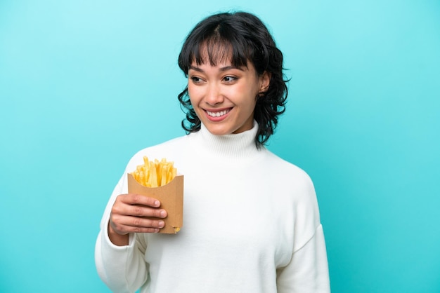 Jeune femme argentine tenant des frites frites isolées sur fond bleu regardant sur le côté et souriant