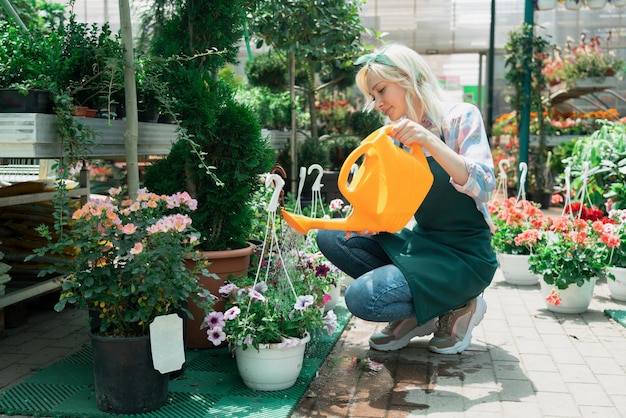 Une jeune femme arrose des fleurs et des plantes dans un jardin.