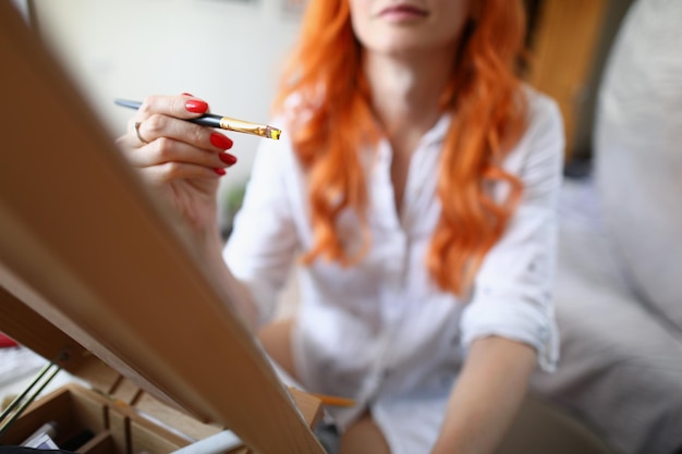 Photo une jeune femme artiste est assise à la maison devant un chevalet avec un pinceau à la main femme apprenant