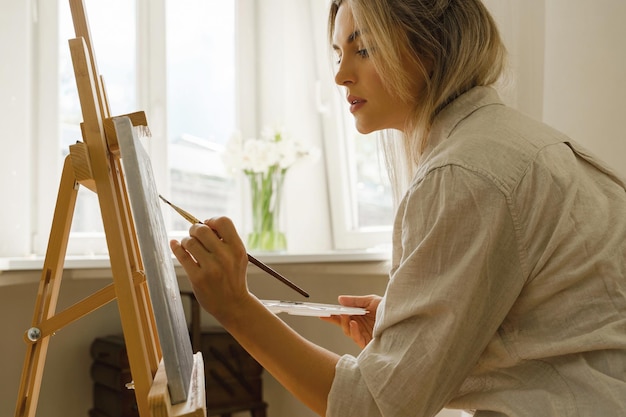 Jeune femme artiste peignant sur toile sur le chevalet au home studio