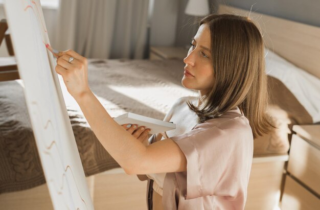 Jeune femme artiste peignant sur toile sur le chevalet à la maison dans le concept d'art et de créativité de la chambre