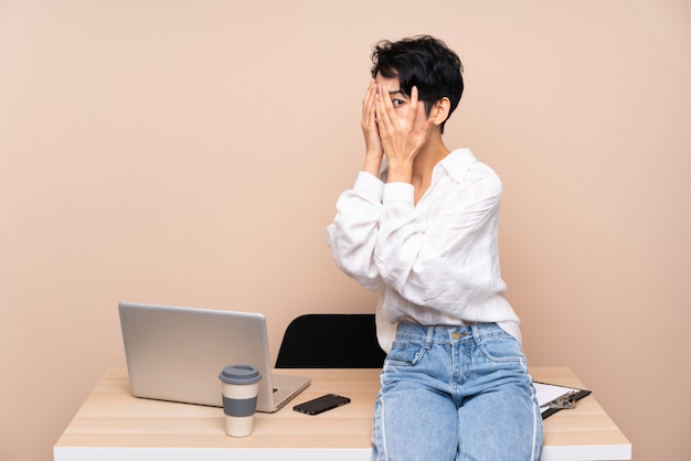 Jeune femme asiatique d'affaires dans son lieu de travail couvrant les yeux et regardant à travers les doigts