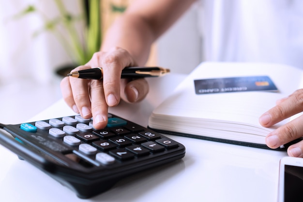 Jeune femme asiatique à l'aide de la calculatrice avec carte de crédit, smartphone et ordinateur portable sur le bureau dans le salon. Travail à domicile concept.