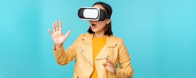 Jeune femme asiatique à l'aide de lunettes de réalité virtuelle à l'aide d'un casque vr debout amusé contre la zone bleue