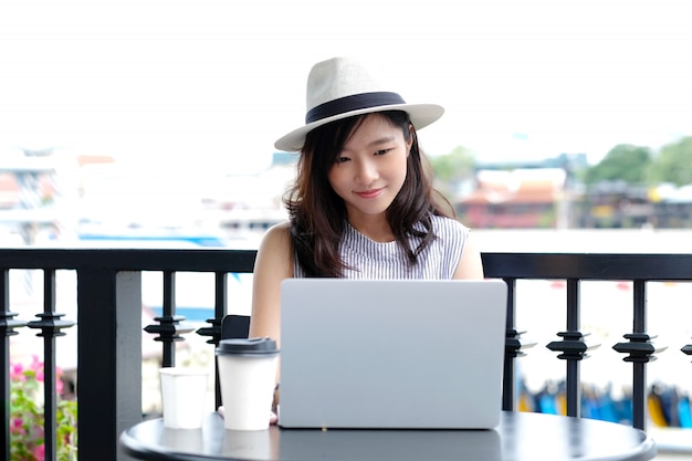 Jeune femme asiatique à l&#39;aide d&#39;un ordinateur portable assis au café en plein air