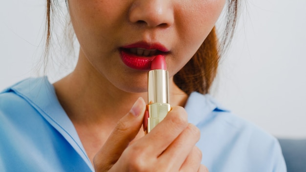 Jeune femme asiatique à l'aide de rouge à lèvres composent dans le miroir avant, femme heureuse à l'aide de cosmétiques de beauté pour s'améliorer prête à travailler dans la chambre à la maison