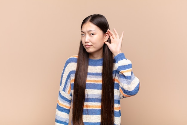 Jeune femme asiatique à l'air sérieuse et curieuse, écoutant, essayant d'entendre une conversation secrète ou des potins, écoutant aux portes