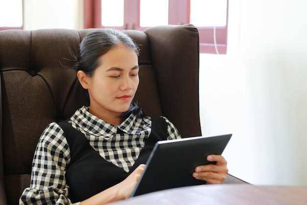 Jeune femme asiatique assise sur le canapé et à l&#39;aide de tablette dans la bibliothèque