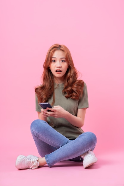 Jeune femme asiatique assise et utilisant un smartphone sur fond rose