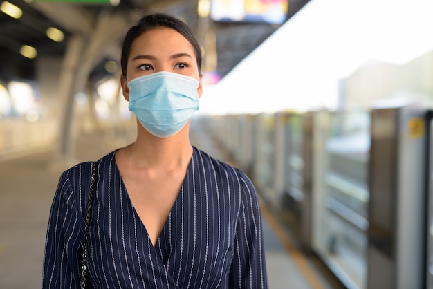 Jeune femme asiatique en attente avec un masque pour se protéger contre l'épidémie de virus corona à la station de skytrain
