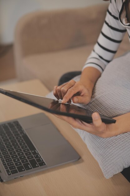 Jeune femme asiatique attrayante se reposant en utilisant la navigation sur l'ordinateur tablette sur le canapé à la maison fille heureuse assise sur le sofa se détendre la lecture de gadget numérique avec excité la communication et le concept de style de vie