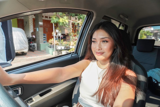 Une jeune femme asiatique attrayante en tenue décontractée sourit en conduisant une voiture.