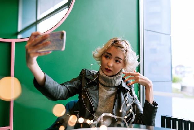 Jeune femme asiatique aux cheveux blonds faisant selfie avec guirlande lumineuse