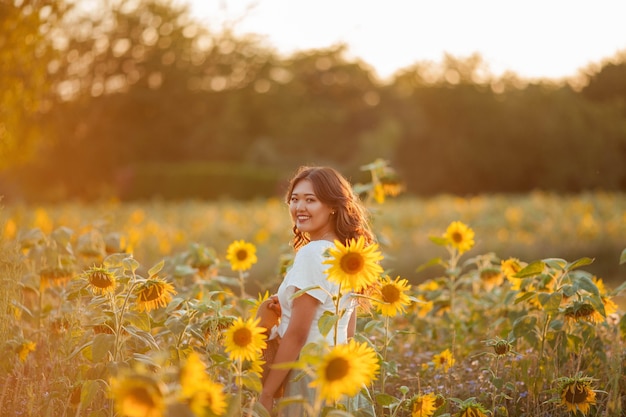 Jeune femme asiatique aux cheveux bouclés dans un champ de tournesols au coucher du soleil.