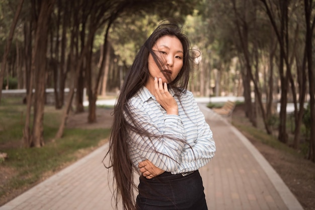 Jeune femme asiatique aux longs cheveux noirs posant dans le parc de la ville en été