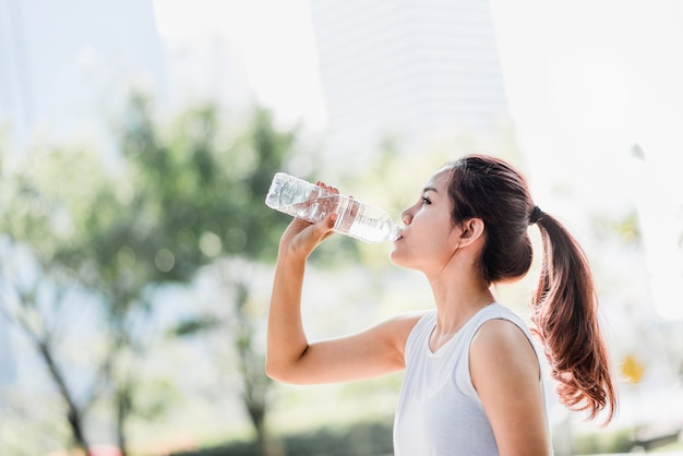 jeune femme asiatique, boire de l&#39;eau de bouteille d&#39;eau après avoir fait du jogging dans le parc