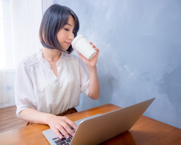 Une jeune femme asiatique boit devant un ordinateur portable