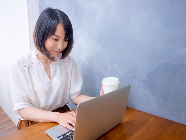 Une jeune femme asiatique boit devant un ordinateur portable