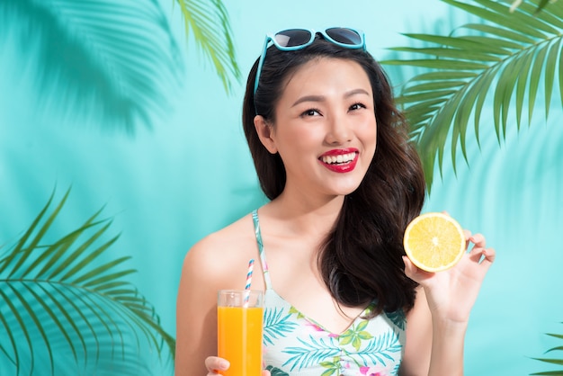 Jeune femme asiatique boit du jus de verre sur fond bleu coloré