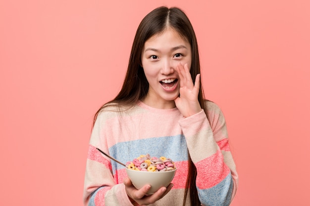 Jeune femme asiatique avec un bol de céréales criant excité à l'avant.