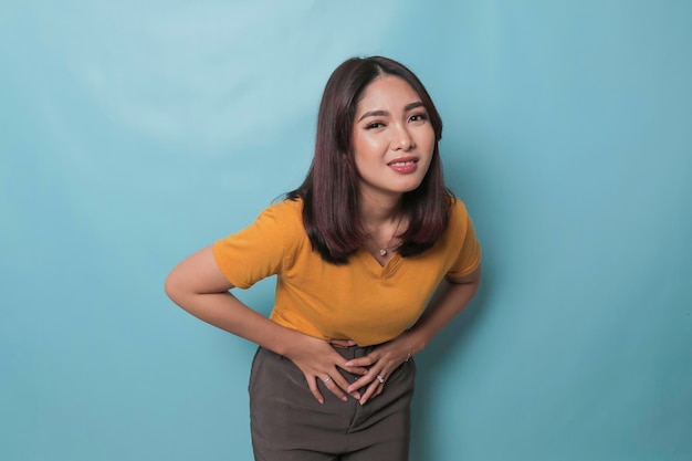 Jeune femme asiatique avec les bras sur le ventre et se penchant avec une expression de maux d'estomac