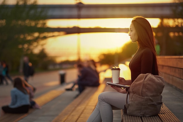 Jeune femme asiatique avec café et livre le soir au coucher du soleil portrait de ville en plein air