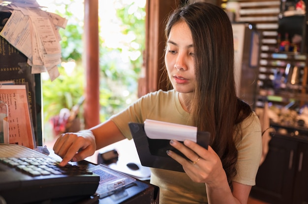 Jeune femme asiatique caissier vérifiant le client de la commande et appuyant sur la caisse enregistreuse au comptoir en bois du restaurant