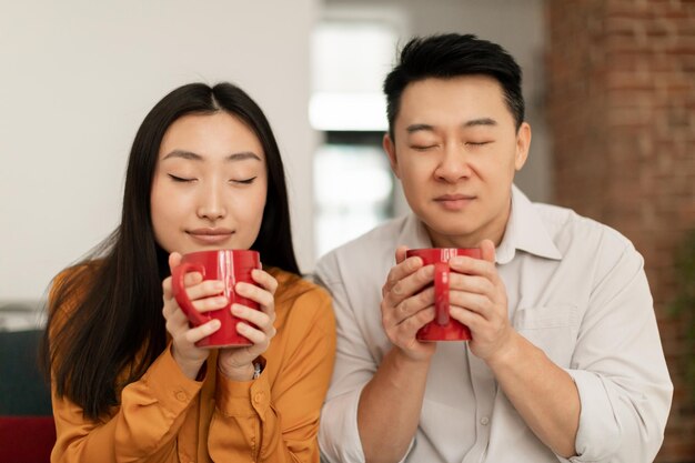 Jeune femme asiatique calme et homme d'âge moyen sentant le café aromatique frais du matin avec les yeux fermés