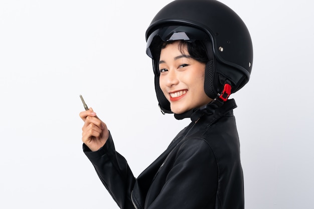 Jeune femme asiatique avec un casque de moto et une clé sur un mur blanc isolé