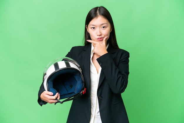 Jeune femme asiatique avec un casque de moto sur fond isolé chroma key pensant
