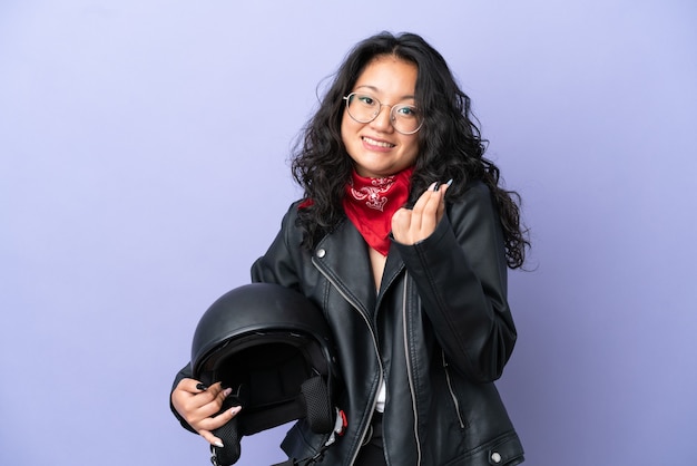 Jeune femme asiatique avec un casque de moto isolé sur fond violet faisant un geste d'argent