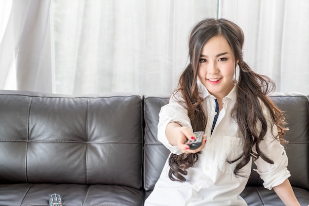 jeune femme asiatique change de chaîne de télévision à la maison dans le salon