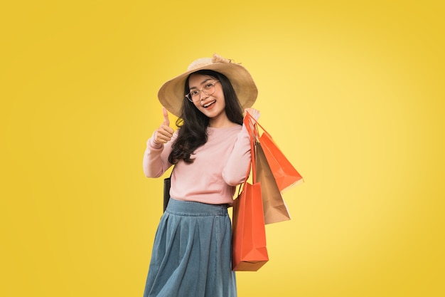 Jeune femme asiatique en chapeau et lunettes transportant un sac en papier avec les pouces vers le haut