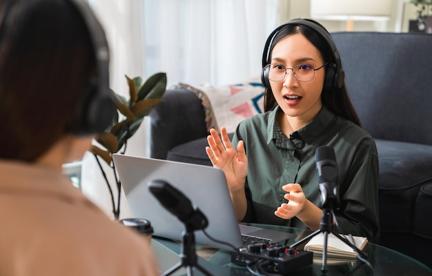 Une jeune femme asiatique en chemise verte utilise des microphones et porte des écouteurs avec une interview de podcast d'enregistrement d'ordinateur portable pour la radio. Concept de créateur de contenu.