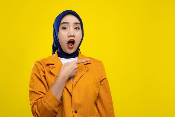 Une jeune femme asiatique choquée montrant du doigt un espace de copie vide avec la bouche ouverte isolée sur un fond jaune