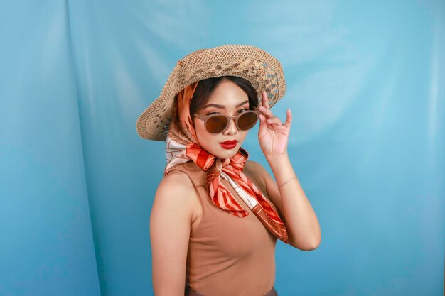 Jeune femme asiatique confiante et heureuse tenant ses lunettes de soleil isolées par un fond bleu