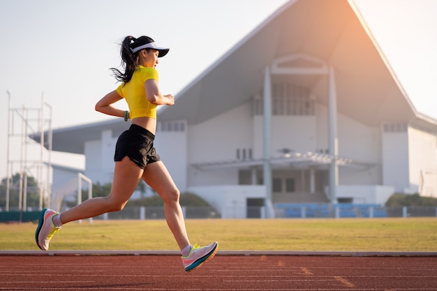 Une jeune femme asiatique coureuse d'athlète faisant du jogging sur une piste de course dans le stade de la ville le matin ensoleillé pour garder la forme physique et un mode de vie sain. La jeune femme de remise en forme s'exécute sur la piste du stade. Sport et loisirs