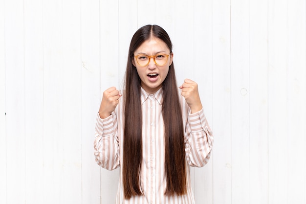 Jeune femme asiatique criant de manière agressive avec une expression de colère ou les poings serrés célébrant le succès