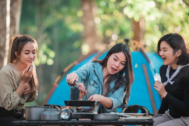 Une jeune femme asiatique cuisine et son amie aime préparer le repas dans la casserole Ils parlent et rient avec plaisir ensemble en camping dans un parc naturel