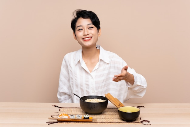 Jeune femme asiatique dans une table avec un bol de nouilles et une poignée de main de sushi après une bonne affaire