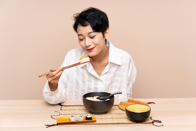 Jeune femme asiatique dans une table avec bol de nouilles et sushi