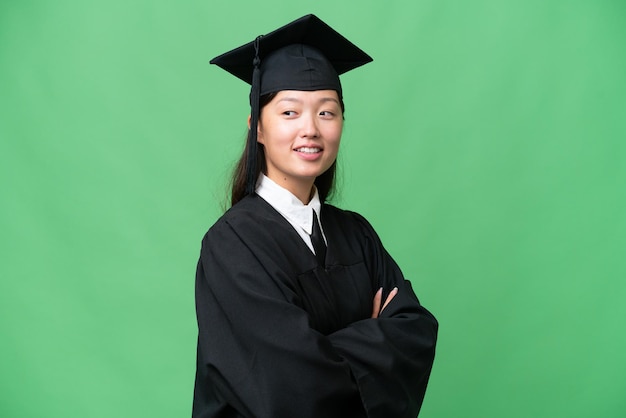 Jeune femme asiatique diplômée de l'université sur fond isolé avec les bras croisés et heureux