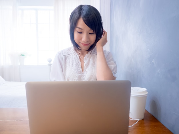 Jeune femme asiatique écoutant des écouteurs devant un ordinateur portable