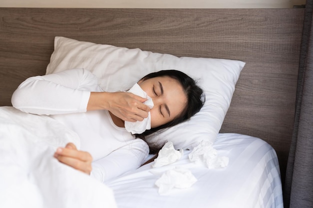 Jeune femme asiatique éternuant symptômes de grippe ou d'allergie se moucher sur le lit après s'être réveillé le matin Concept d'allergie et d'asthme