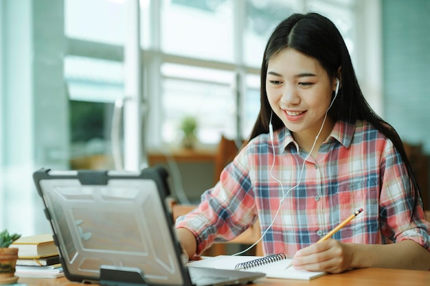 Une jeune femme asiatique étudie devant l'ordinateur portable et utilise des écouteurs au bureau.