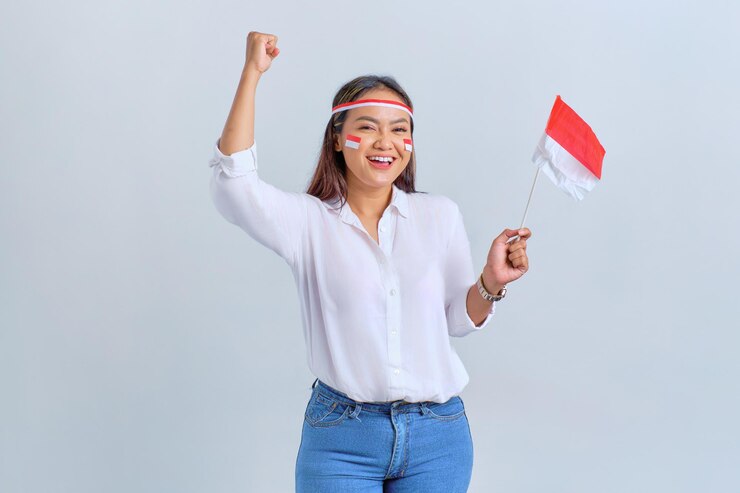 Une jeune femme asiatique excitée célèbre le jour de l'indépendance indonésienne tenant le drapeau indonésien isolé sur fond blanc